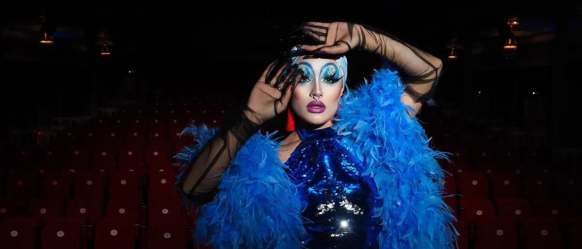 Drag performer with a blue feather boa in a theater