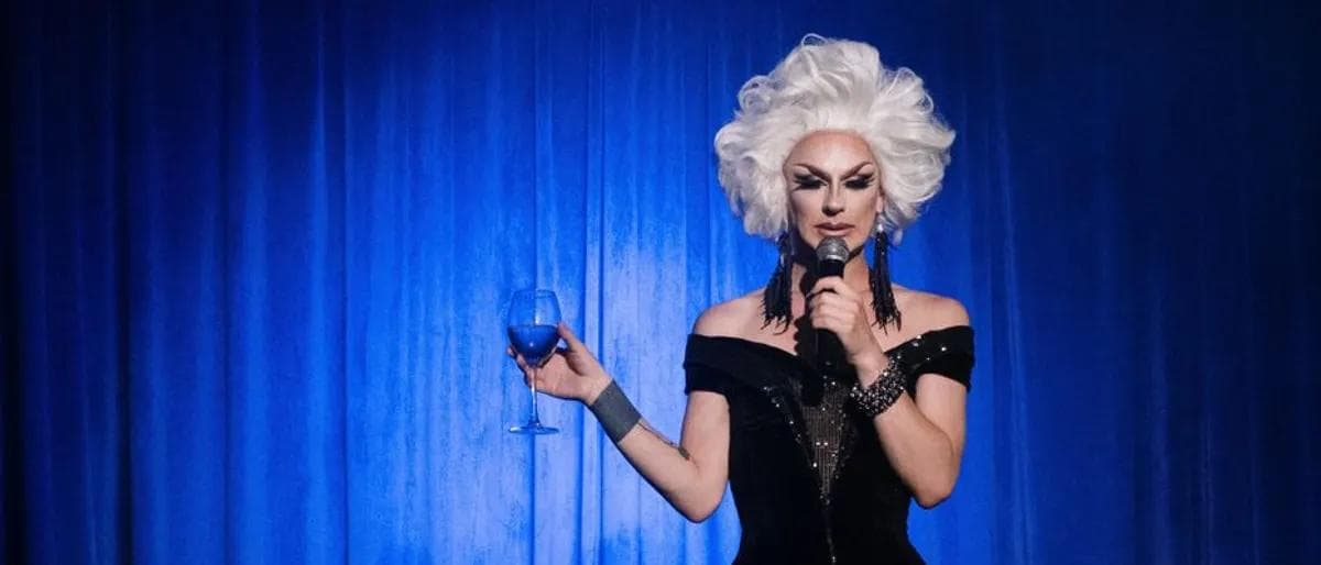 Drag performer holding a cocktail glass on stage
